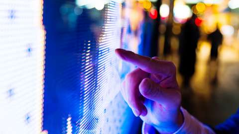 Jari pria menunjuk layar LED harga pasar saham di malam hari